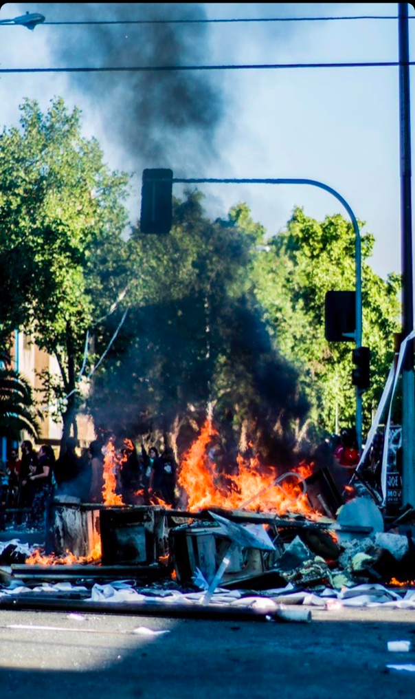 Image from @matiasjofrem showing a fire burning in front of protestors in Santiago